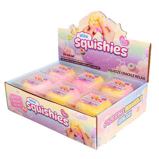 A retail display box filled with small packaged squishies. The display is pastel pink, purple, and blue with the brand name 'Wax' and product name 'Squishies' prominently printed on the packaging.
