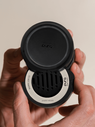 Person holding a black and silver Pura product against a beige background